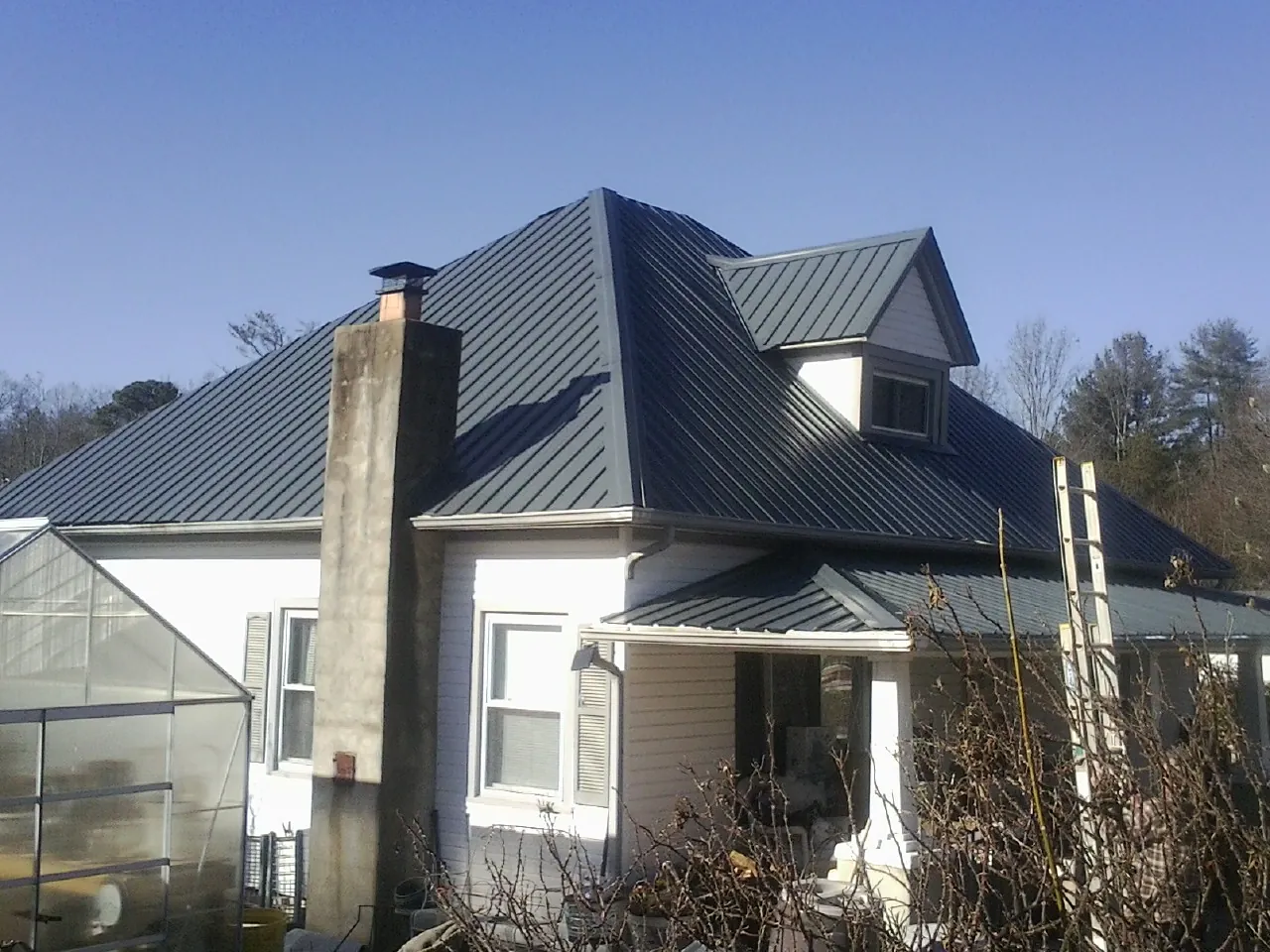 Dark blue standing seam metal roof on a white farmhouse with dormer — Slate & Tile Roof Repair by Roofing Brothers in Broxton