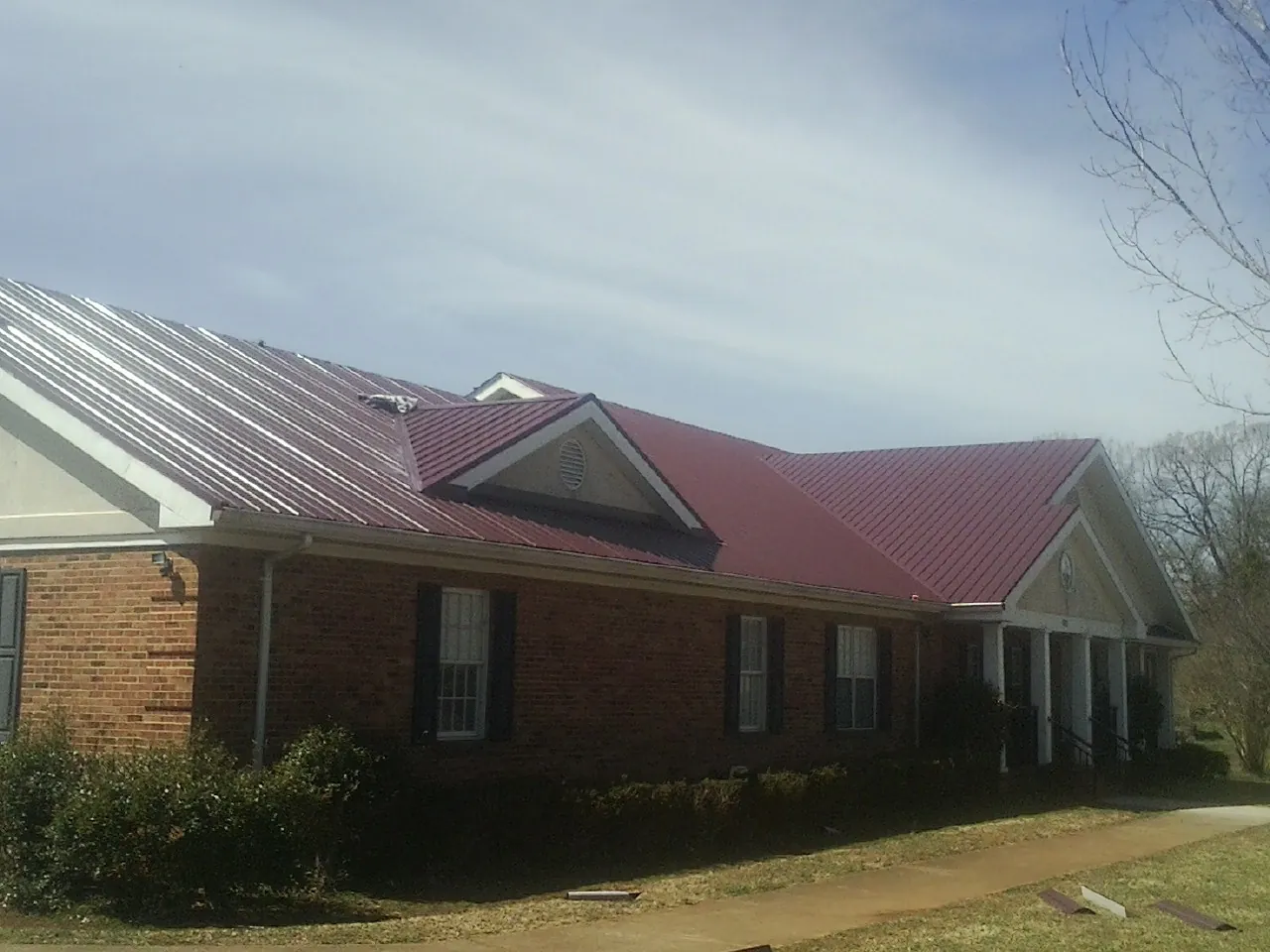 Red metal roof with gabled entries on a long brick building, from a Hail Damage Roof Repair job in Broxton