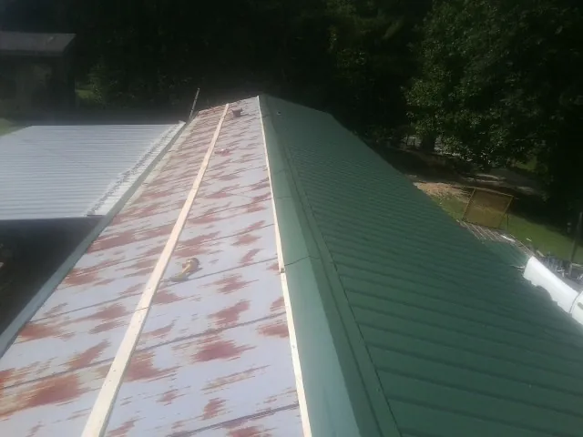 Old rusted panels beside newly installed green metal roofing — Wind Damage Roof Repair by Roofing Brothers in Broxton