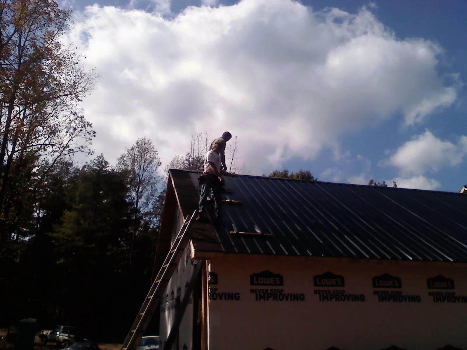 Roofer fastening dark metal panels high against a cloudy sky, from a Roof Inspection job in Broxton