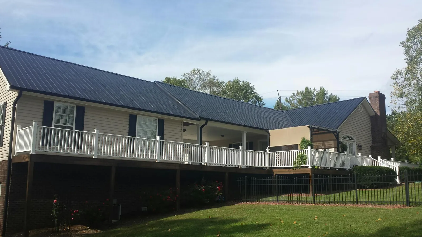 Black metal roof above a long white railed deck on a hillside home in Broxton