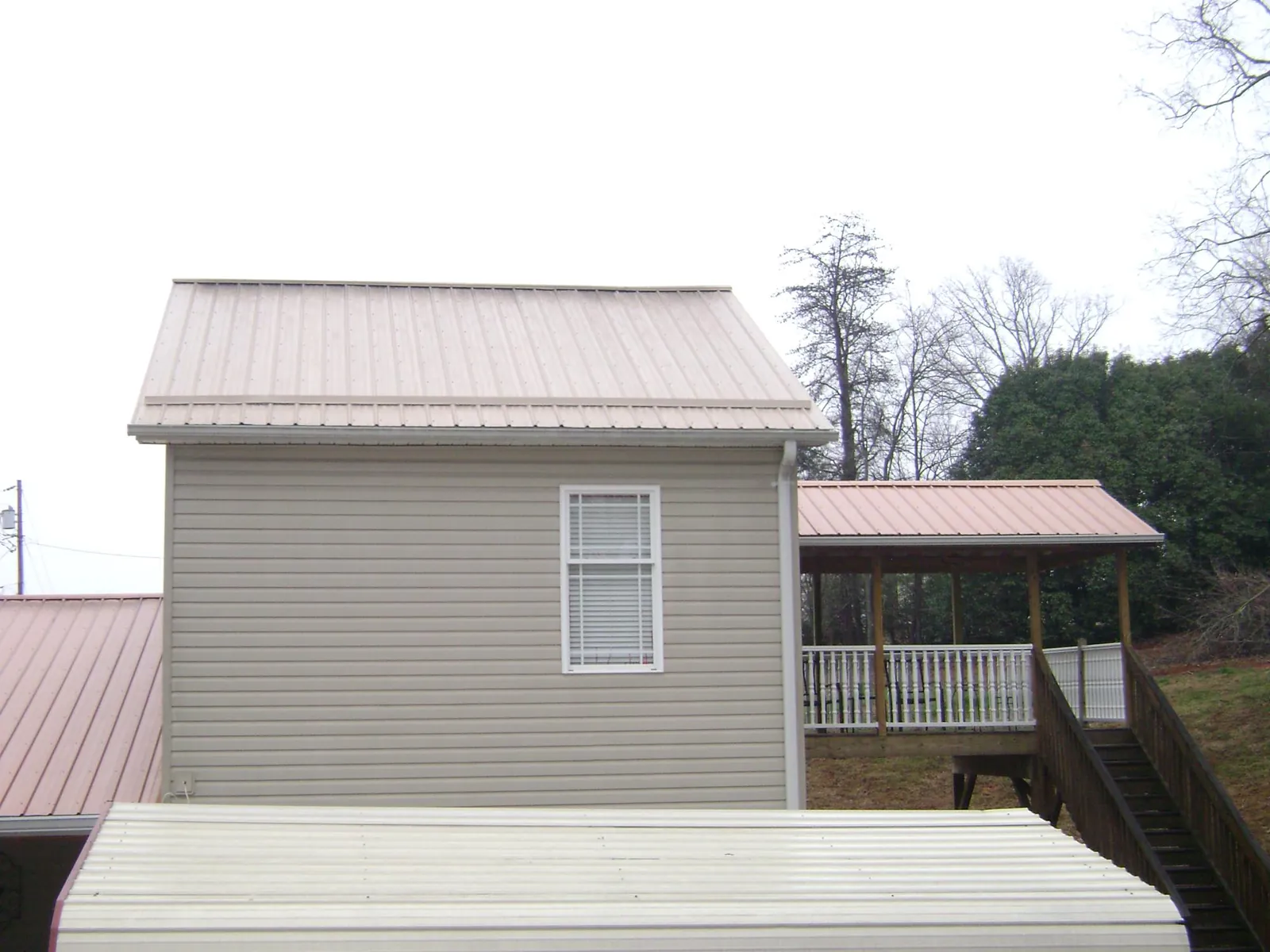 Tan metal roofs on a two story addition and attached porch, from a Roof Replacement job in Broxton